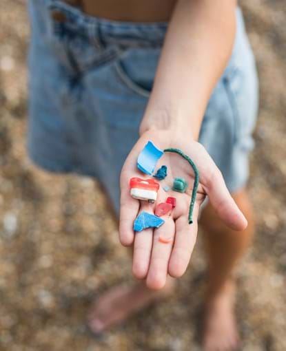 Child's hand holding pieces of plastic pollution
